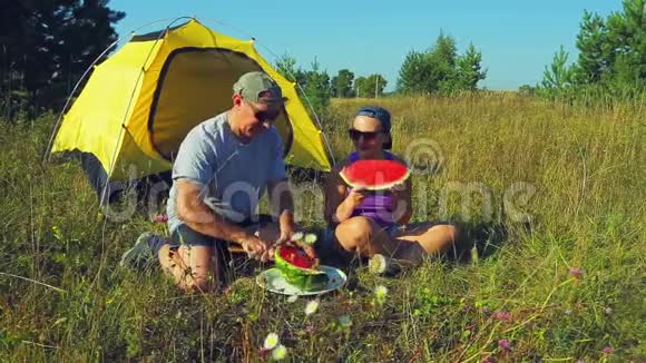 幸福的男人和女人在森林里的帐篷附近一个人用刀子在大块上切西瓜视频的预览图
