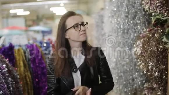在超市里戴着眼镜的漂亮女孩看着圣诞花环的架子视频的预览图