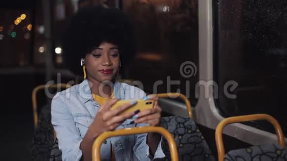 年轻的非洲裔美国妇女在公共交通工具上看智能手机视频晚上特写镜头城市视频的预览图