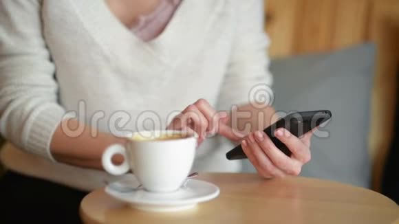 女人在餐桌上写作喝咖啡或茶她端着杯子看着智能手机特写视频的预览图