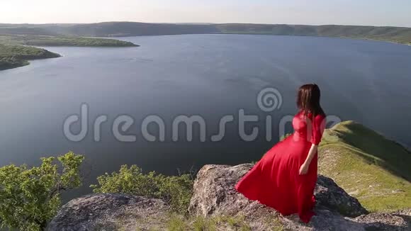 美丽的黑发女人穿着红色的裙子在巨大的河岸边为相机摆姿势视频的预览图