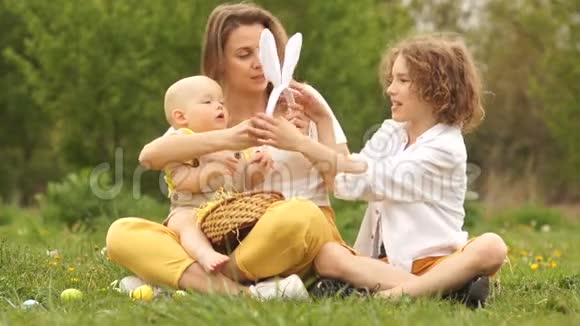 妈妈和她的两个儿子在草地上复活节野餐兔子服装快乐的复活节家庭视频的预览图