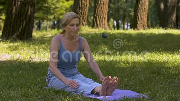 年轻的女士在公园的垫子上伸展瑜伽业余的好的形状缓慢的运动视频的预览图