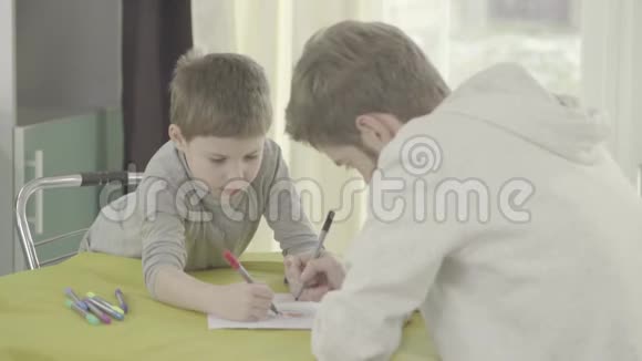 父亲和儿子坐在客厅的桌子上画纸父子关系视频的预览图