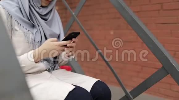 戴头巾的年轻女子坐在外面的楼梯上发短信向上倾视频的预览图