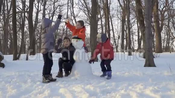 在冬天的公园里玩耍的孩子们在雪人的附近互相嬉戏视频的预览图
