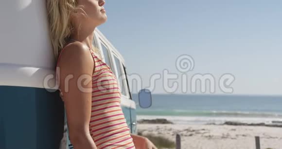 一位年轻女子靠在海边的露营车上视频的预览图
