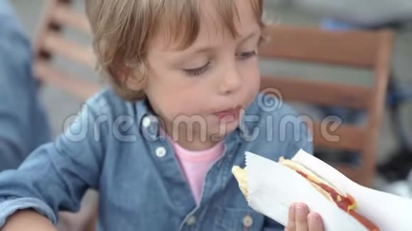 五岁的男孩穿着牛仔衬衫吃美味的热狗视频的预览图