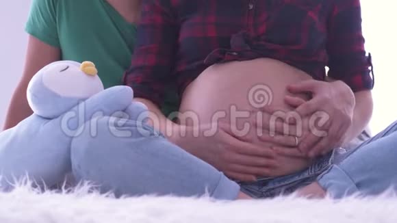 男人的手把女人的肚子擦得紧紧的情侣坐在蓬松的表面企鹅玩具靠近视频的预览图