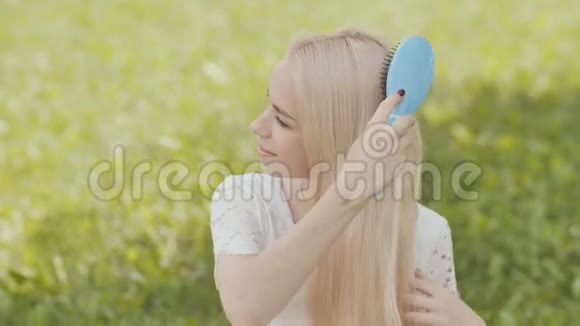 坐在公园的草地上的俄罗斯金发女孩被梳理着视频的预览图