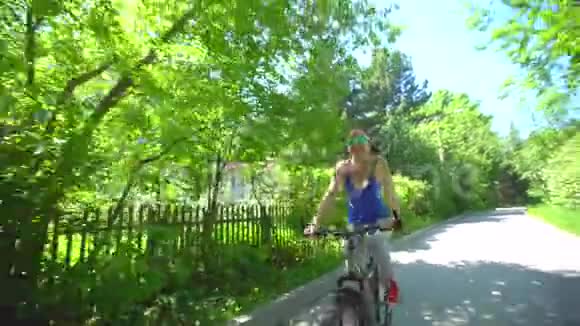 在温暖的夏天美丽运动的年轻女人以快乐和积极的方式骑自行车戴眼镜的女孩视频的预览图