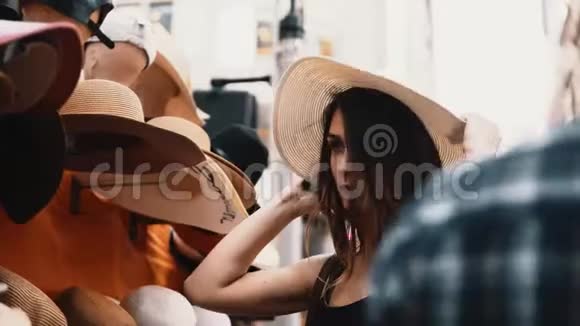 年轻漂亮的女人在街上的商店里试穿帽子有魅力的女性去市中心购物视频的预览图