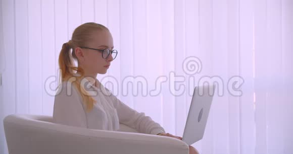 特写侧景照片年轻漂亮的白种人金发女商人戴着眼镜用笔记本电脑看相机视频的预览图