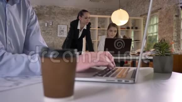办公室里摆着一杯咖啡商人的手在笔记本电脑上打字他的同事们正在与视频的预览图