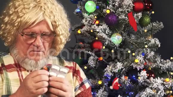 戴着灰色胡子的快乐老人在花环的圣诞树背景上吃着带水的药和饮料片绿色视频的预览图