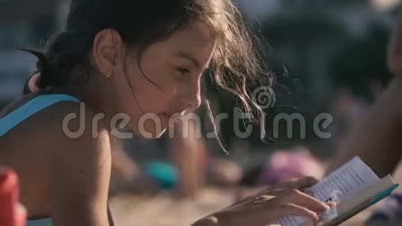 年轻女孩穿着泳衣在海边沙滩上看书4K视频的预览图