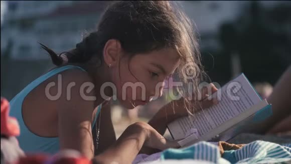年轻女孩穿着泳衣在海边沙滩上看书4K视频的预览图
