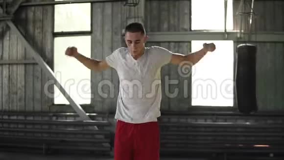 年轻的白种人男拳击手跳跃和伸展手臂热身在健身房周围的拳击袋体育拳击视频的预览图