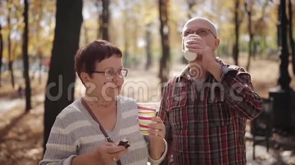 秋天公园里的一对老夫妇在塑料杯里聊天喝咖啡或茶视频的预览图