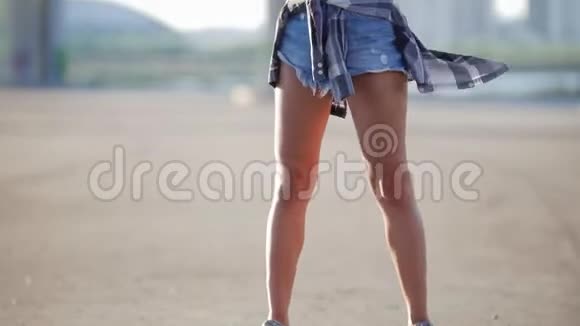 一个穿着短短裤的漂亮女孩腰带上的一件t恤和一件格子衬衫拿着一个溜冰鞋看着相机视频的预览图