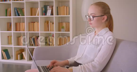 特写侧景照片年轻漂亮的白种人金发女商人戴着眼镜用笔记本电脑看相机视频的预览图