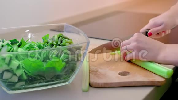 特写镜头动作缓慢无法辨认的女人把芹菜片放在木板上放入一个大厨房的玻璃沙拉碗里视频的预览图