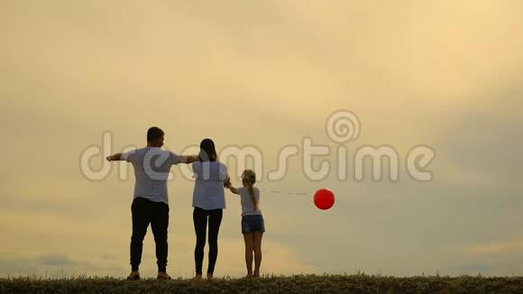 在日落的背景下年轻的母亲和父亲带着女儿在草地上笑着玩气球快乐的爱视频的预览图