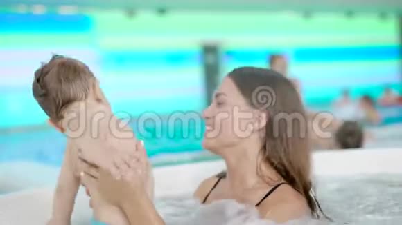微笑的黑发女人和可爱的小男孩在水疗中心享受按摩浴缸视频的预览图