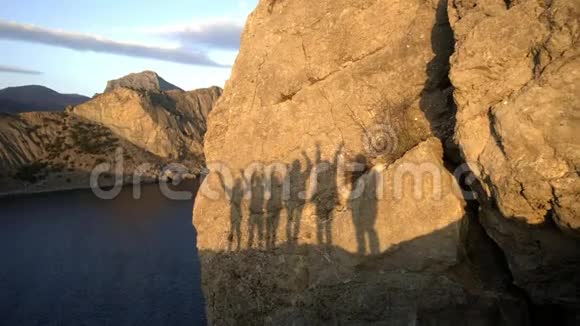 一群多民族朋友挥舞着手的剪影日落时在海中的岩石上剪影享受享受乐趣视频的预览图