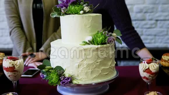 两层白色蛋糕上面装饰着鲜花反对人们说话视频的预览图