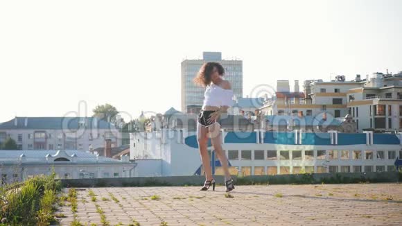 迷人的穆拉托年轻女子性感地穿着高跟鞋在屋顶上跳舞视频的预览图