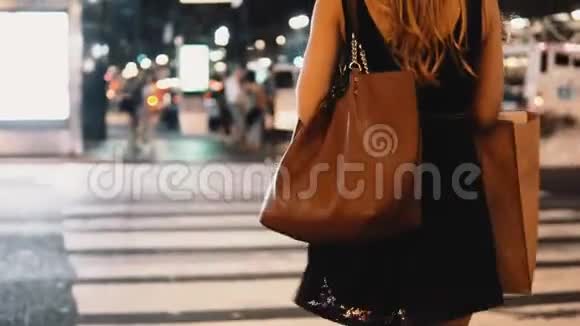 晚上在纽约美国市中心带着购物袋穿过马路的年轻时尚女性的特写镜头视频的预览图