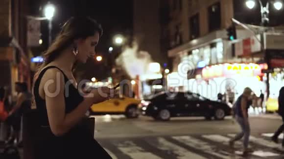 年轻漂亮的女人站在市中心靠近纽约的十字路口使用智能手机视频的预览图