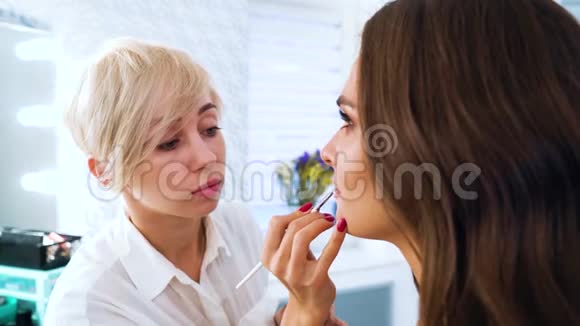 美妆师在美容院用刷子将唇彩涂在年轻女子脸上视频的预览图