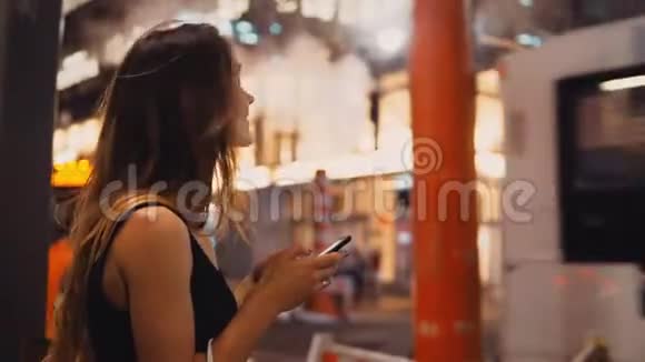 年轻快乐的女人带着购物袋站在纽约市中心交通的烟斗附近使用智能手机视频的预览图