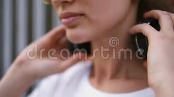 年轻的高加索女人在阳光明媚的夏日带着黑色耳机穿着黄色衣服听音乐的女孩视频的预览图