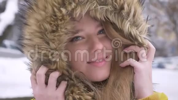 在冬季街头一幅美丽的年轻白种人女孩的特写肖像她穿着毛皮帽在镜头前调情视频的预览图