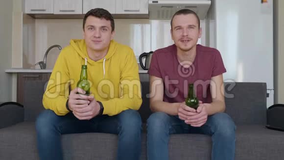 两个人坐在沙发上看电视上的足球赛喝啤酒视频的预览图