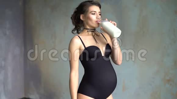 孕妇从杯子里贪婪地喝牛奶4K的灰色墙底上美丽的黑发少女视频的预览图