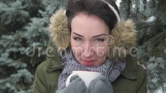 女人在冬天的森林里喝热茶或咖啡她头上戴着毛皮耳罩美丽的风景雪碧视频的预览图
