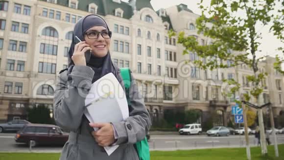 自信微笑的穆斯林女学生站在街上打电话视频的预览图