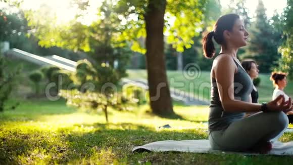 女人坐在瑜伽垫上摆出莲花的姿势日出时在公园里沉思视频的预览图