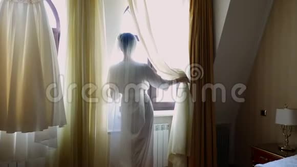 一个新娘美丽的女孩戴着面纱穿着白色长袍望着窗外新娘的早晨视频的预览图