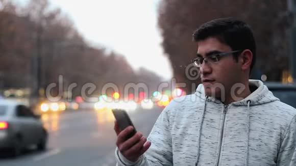 一个戴着眼镜穿着白色衬衫的人在电话里说着话在汽车前灯的背景下生气视频的预览图