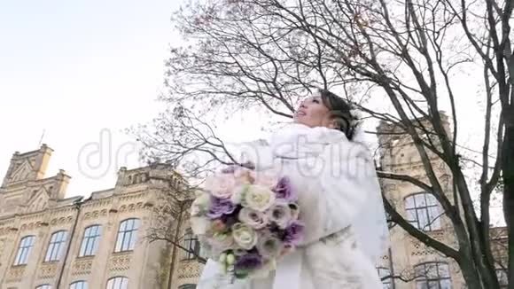 美丽新娘的肖像穿着白色连衣裙面纱和毛皮外套捧着婚礼花束的背景视频的预览图
