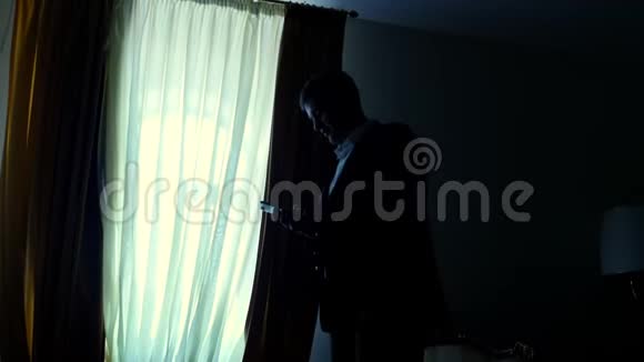 黄昏时分在黑暗中窗外穿着白色衬衫和蓝色夹克的商人手里拿着视频的预览图