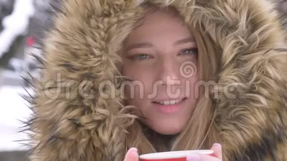 在冬季街头背景下用热饮观看镜头拍摄年轻女孩的特写肖像视频的预览图