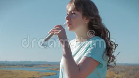 欧洲的女人出现在露天的饮料水从瓶子对抗一个晴朗的蓝天健康的生活方式视频的预览图