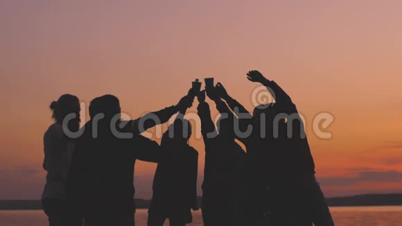 慢动作的剪影团体年轻的舞蹈者欢呼并在日落的海滩上举行派对视频的预览图