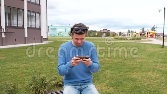 男人在家附近坐在长凳上玩手机游戏视频的预览图